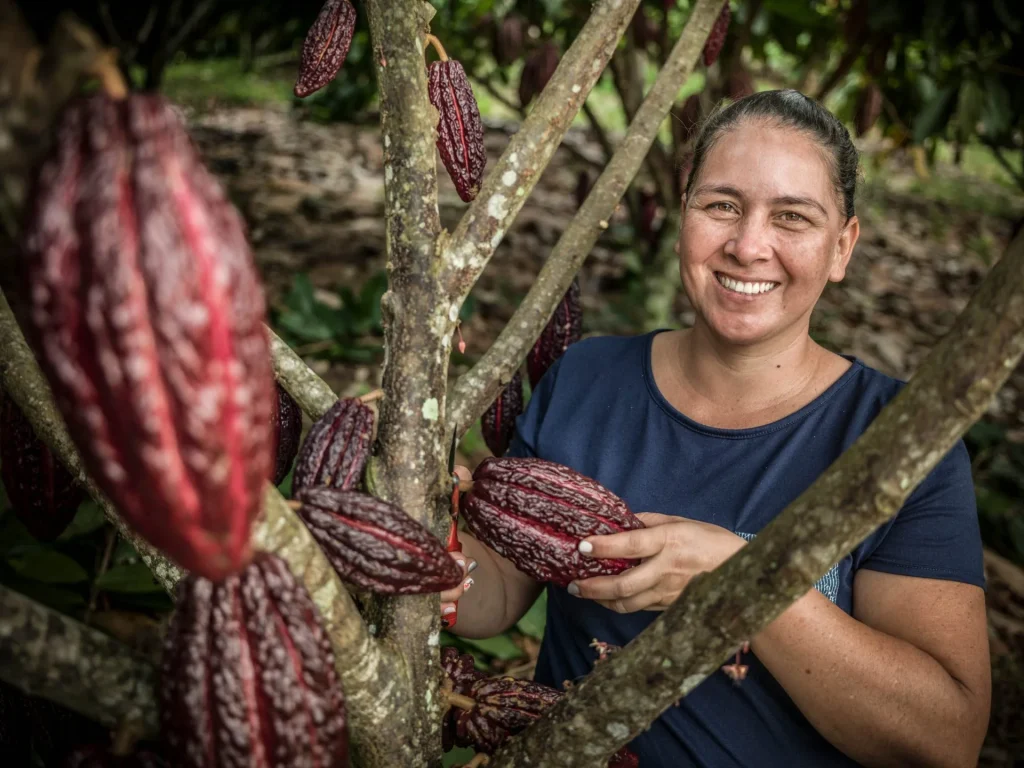 Mujer sosteniendo una mazorca de cacao en medio de un cultivo con origen sostenible en Colombia